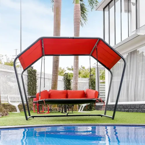 Metallschaukelstuhl mit rotem Dach und Polstern neben einem Pool im Garten.