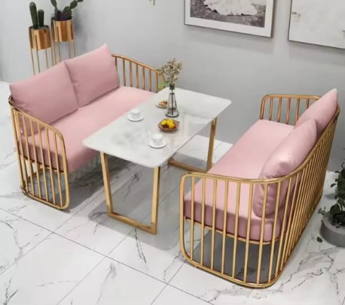 Canapés de réception modernes avec coussins roses et cadre doré, autour d'une table en marbre.