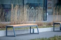 Amager 4-personers offentlig bænk uden ryglæn, stående udendørs nær en glasbygning.