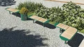 A green Nordhavn Outdoor Planter | 55 l with yellow flowers, placed next to wooden benches in a garden.