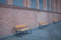 Offentlig bænk Amager 4-personers med ryglæn og armlæn foran murstensvæg