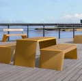 Gul Nyboder 3-personers offentlig bænk uden ryglæn på terrasse med udsigt over havet.