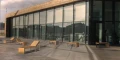 Moderne træbænke uden ryglæn foran en glasbygning.