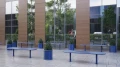 Banc public sans dossier Sydhavn 4 places en métal bleu sur une place moderne avec plantes en pots.