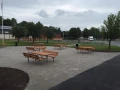 Banc et table en acier galvanisé sur une place publique, entourés d'arbres et de bâtiments.