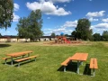 Bænk &amp; bord (galvaniseret stål) på grøn græsplæne ved legeplads.