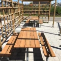 Outdoor seating area with wooden benches and tables on galvanized steel frames.