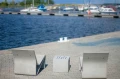 Concrete cube with geometric design between two modern outdoor chairs by the waterfront.